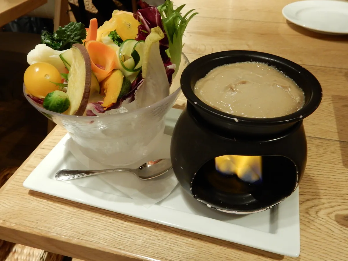 Bagna cauda calda nel fornelletto con la fiammella, accanto a una coppa di verdure crude