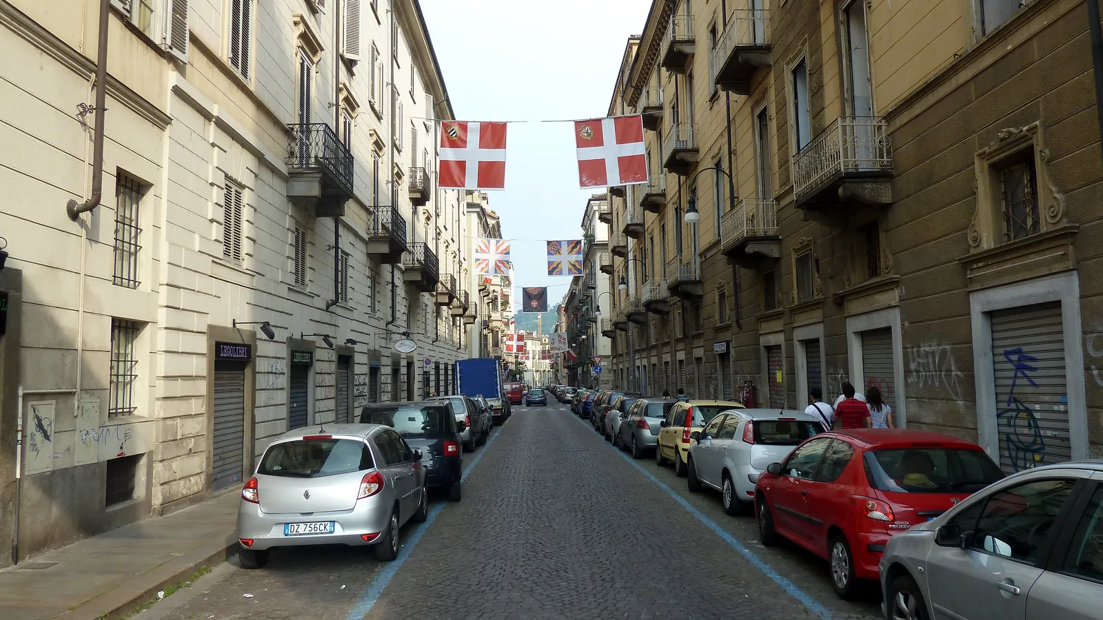 Parcheggio sulle strisce blu in una via lastricata del centro di Torino, con auto in sosta